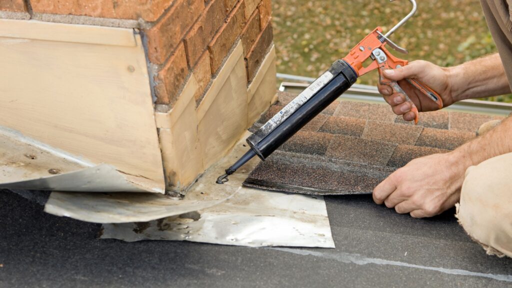 Roofer Applying Caulk to House Chimney Flashing