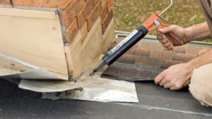 Roofer Applying Caulk to House Chimney Flashing
